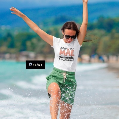 Mulher com t-shirt branca com texto e calções verdes brincando na praia