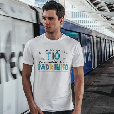 Homem com camisola branca e texto em português na plataforma de estação de metro com comboio ao fundo