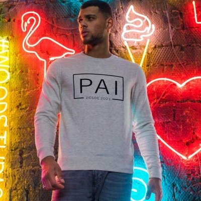 Homem com camisola cinza 'PAI DESDE 2021' em frente a parede com luzes neon coloridas