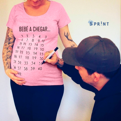 Pessoa grávida com t-shirt rosa com calendário de gravidez, outra pessoa marca número com caneta