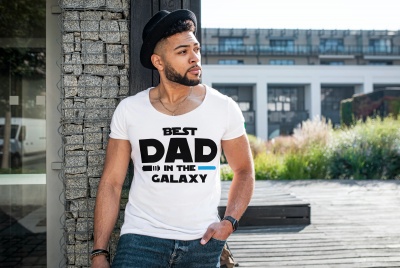 Homem usando camisola branca com texto 'BEST DAD IN THE GALAXY' encostado a coluna de pedra