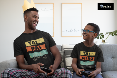 Pai e filho sorridentes sentados no sofá usando t-shirts pretas combinando a jogar videojogos.