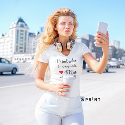 Mulher loira com t-shirt branca com texto e headphones dourados a tirar selfie na rua