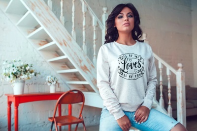 Mulher com sweatshirt cinza e calças jeans sentada em ambiente com escada branca e móveis coloridos