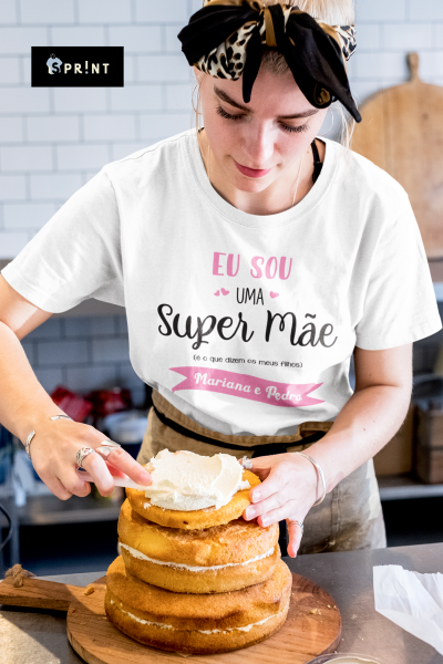 Mulher a decorar bolo com t-shirt personalizada 'Super Mãe' numa cozinha