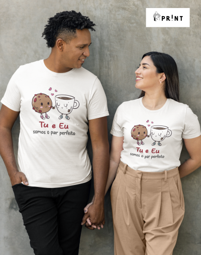 Casal com t-shirts brancas ilustradas com bolacha e chá e texto romântico em português, posando em fundo cinzento.