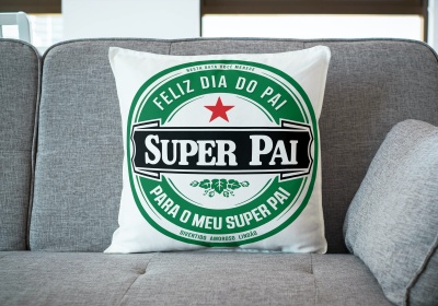 Almofada branca com estampa verde e preta 'SUPER PAI' num sofá cinzento