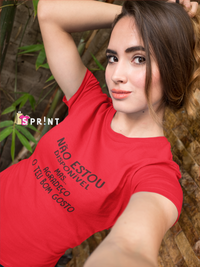 Mulher com t-shirt vermelha com texto preto, em ambiente exterior com plantas e parede de pedra