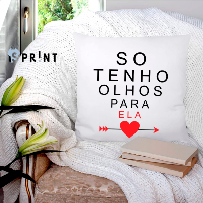 Almofada branca com texto em preto e vermelho sobre sofá bege com manta branca e livros