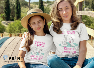 Duas pessoas usando t-shirts brancas com desenhos de gatos e textos em português sentadas ao ar livre