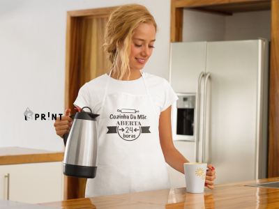 Mulher com avental branco 'Cozinha Da Mát ABERTA 24 horas' segurando jarro térmico e caneca na cozinha