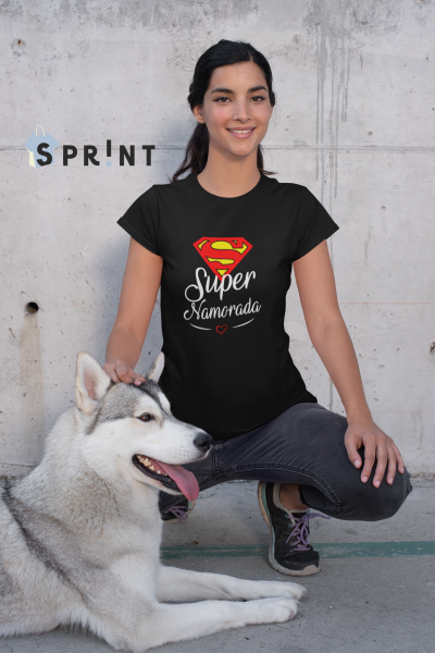 Mulher com t-shirt preta 'Super Namorada' e cão husky sentado junto a parede de cimento