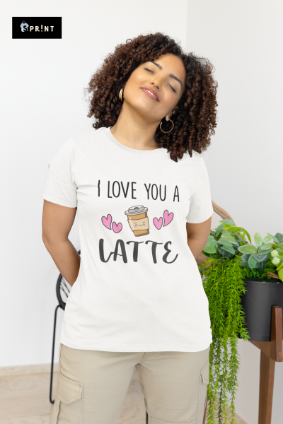 Mulher a usar t-shirt branca com estampa 'I LOVE YOU A LATTE' e calças bege, em ambiente interior com plantas.
