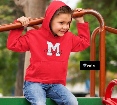 Criança com camisola vermelha com capuz e estampa 'M Miguel', sentada em parque infantil
