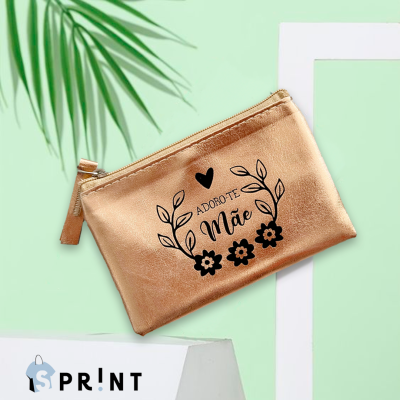 Necessaire bronze metálica com texto 'ADORO-TE Mãe' e decoração preta, em fundo verde com folhas e suporte branco