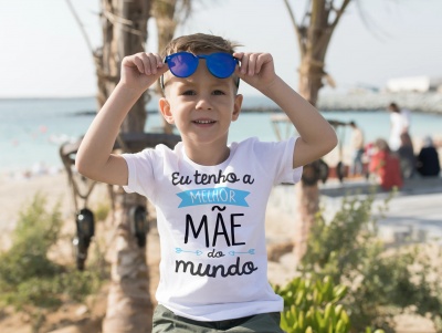 Camiseta branca com texto em português usada por menino na praia