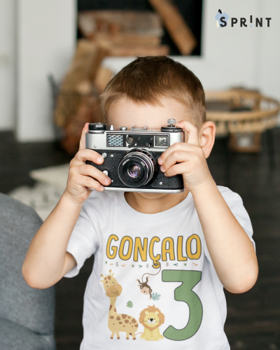 Criança com camisola branca estampada segurando uma câmara fotográfica vintage cinzenta e preta