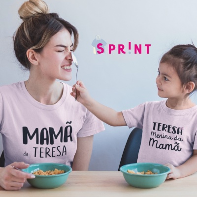 Mulher e menina com t-shirts rosa claro com textos relacionados a mãe e filha sentadas à mesa com tigelas de comida