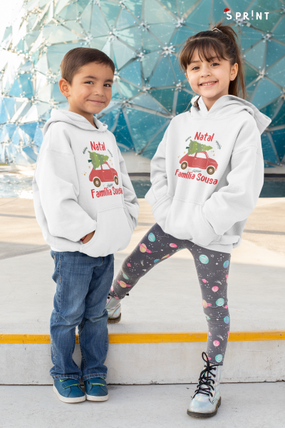 Duas crianças com sweatshirts brancas com capuz estampadas com carro vermelho e árvore de Natal verde em ambiente exterior