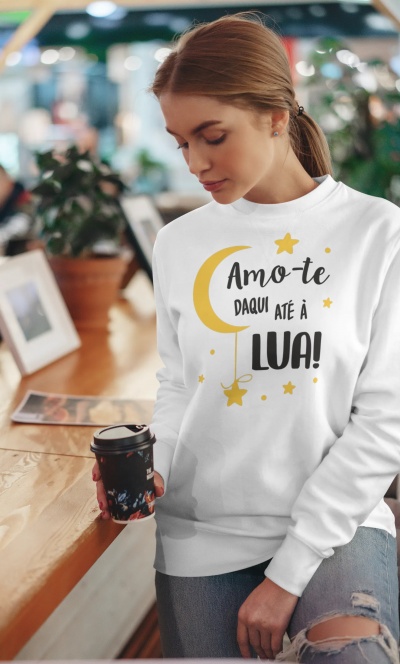 Pessoa com camisola branca estampada 'Amo-te daqui até à LUA!' segurando copo de café num interior