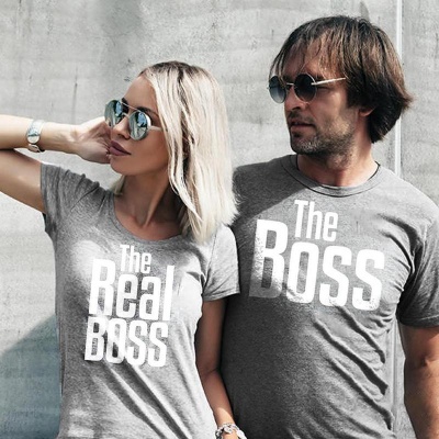Casal usando t-shirts cinzentas com textos 'The Real BOSS' e 'The BOSS', com óculos de sol, junto a uma parede cinzenta.