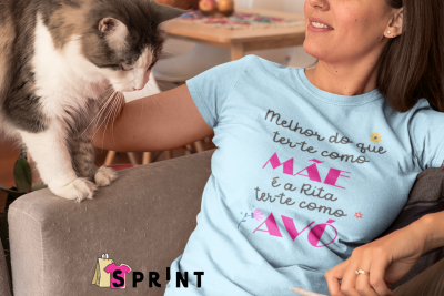 T-shirt azul clara com texto em português, mulher sentada num sofá com gato ao lado