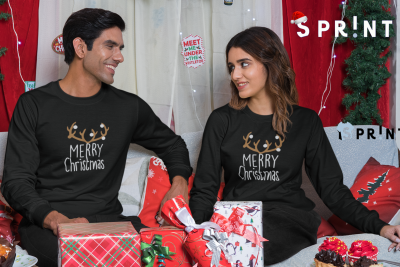 Homem e mulher vestidos com camisolas natalícias pretas, sentados com presentes de Natal ao redor em ambiente decorado para Natal.