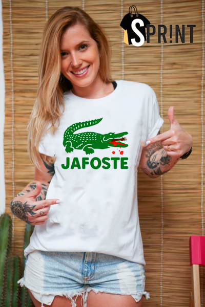 Mulher sorridente com t-shirt branca com estampa de crocodilo e texto JAFOSTE, shorts de ganga, fundo cortina bambu