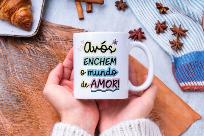 Caneca branca com texto colorido segurada nas mãos, ao lado de croissant e especiarias