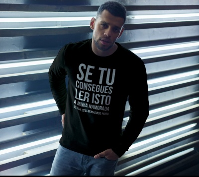 Homem com camisola preta com texto branco e calças de ganga encostado a estrutura metálica prateada com luzes.