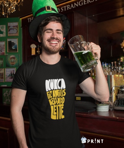 Homem com camiseta preta com texto em branco e amarelo segurando caneca de bebida verde em bar