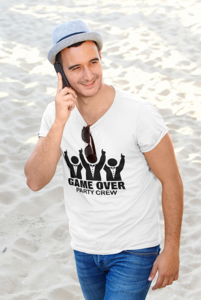Homem na praia a usar t-shirt branca com texto 'GAME OVER PARTY CREW' e chapéu cinzento
