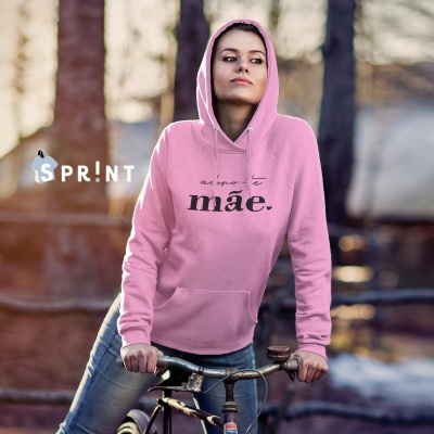 Mulher com capuz rosa claro de casaco com texto a preto, segurando bicicleta ao ar livre