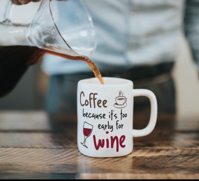 Caneca branca com texto e ilustrações de café e vinho, sendo enchida com café.