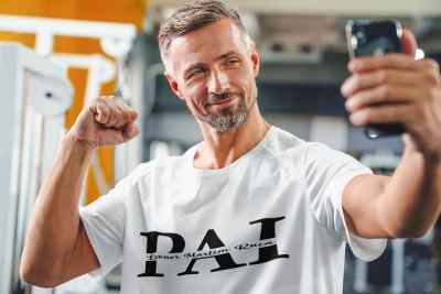 Homem a usar t-shirt branca com texto preto, a tirar uma selfie num ginásio