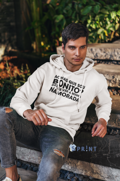 Homem com sweatshirt branca com capuz e texto em preto sentado em escadas de pedra junto a vegetação