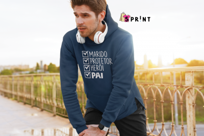 Homem com casaco azul com texto sobre papelaria e auriculares brancos ao ar livre junto a vedação metálica.