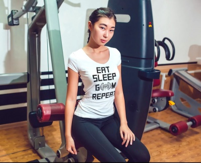 Mulher sentada num banco de ginásio a usar camisola branca com texto e calças pretas