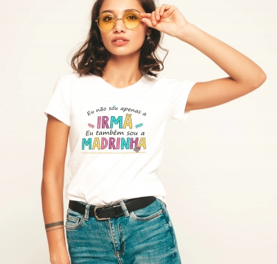 Mulher com t-shirt branca com texto colorido em português, calças de ganga e óculos amarelos.