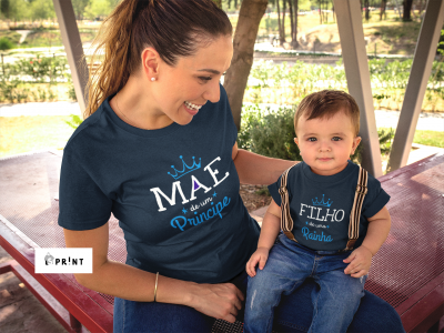 Mãe e filho vestidos com t-shirts azuis escuras com textos relacionados a príncipe e rainha, sentados num parque.