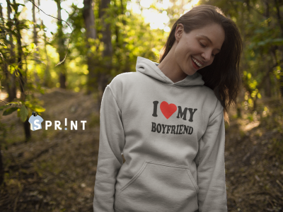 Mulher sorridente de sweatshirt cinza claro com capuz e texto I ❤️ MY BOYFRIEND, em floresta.