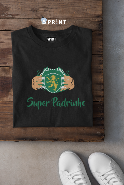 Camiseta preta com estampa Sporting Super Padrinho sobre fundo de madeira e ténis brancos ao lado