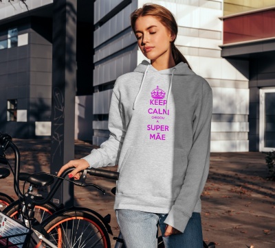 Mulher com sweatshirt cinzenta com texto rosa 'KEEP CALM E SEJA UMA SUPER MÃE' junto a bicicleta preta