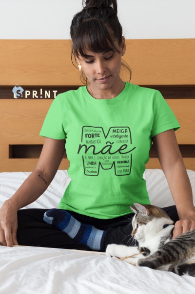 Mulher com t-shirt verde clara com texto em preto sentado numa cama ao lado de um gato branco e cinzento