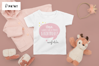 T-shirt branca infantil com frase e balão rosa numa superfície rosa com casaco de malha, botas, tiara e peluche