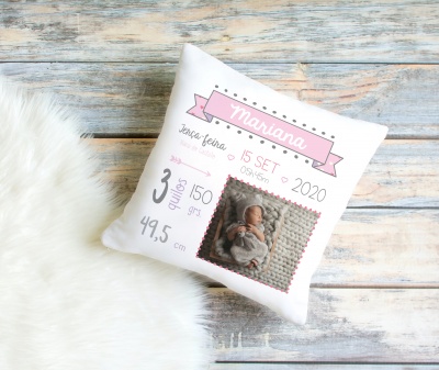 Almofada branca personalizada com dados de nascimento e foto de bebé sobre superfície de madeira e tapete branco