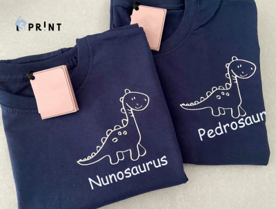 Duas t-shirts azuis escuras com dinossauro branco e nomes Nunosaurus e Pedrosaurus
