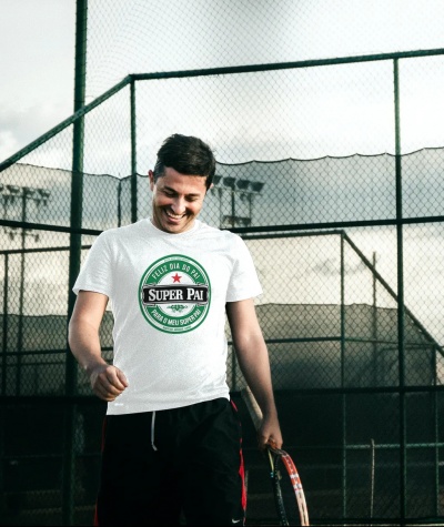 Homem com t-shirt branca com mensagem dia do pai, calça preta, segurando raquete de ténis numa quadra de ténis