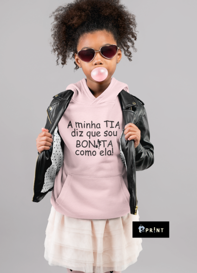 Criança com hoodie rosa e casaco de cabedal preto, com óculos escuros, a fazer bolha com pastilha elástica.