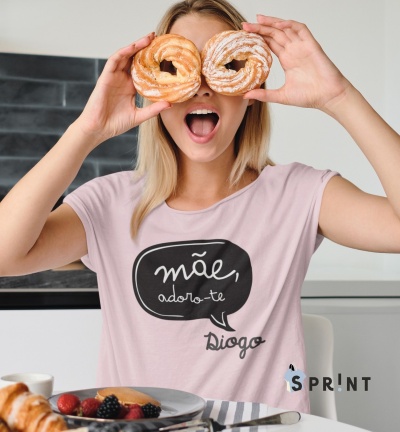 Pessoa segurando dois doces, t-shirt rosa com texto e mesa com frutas.